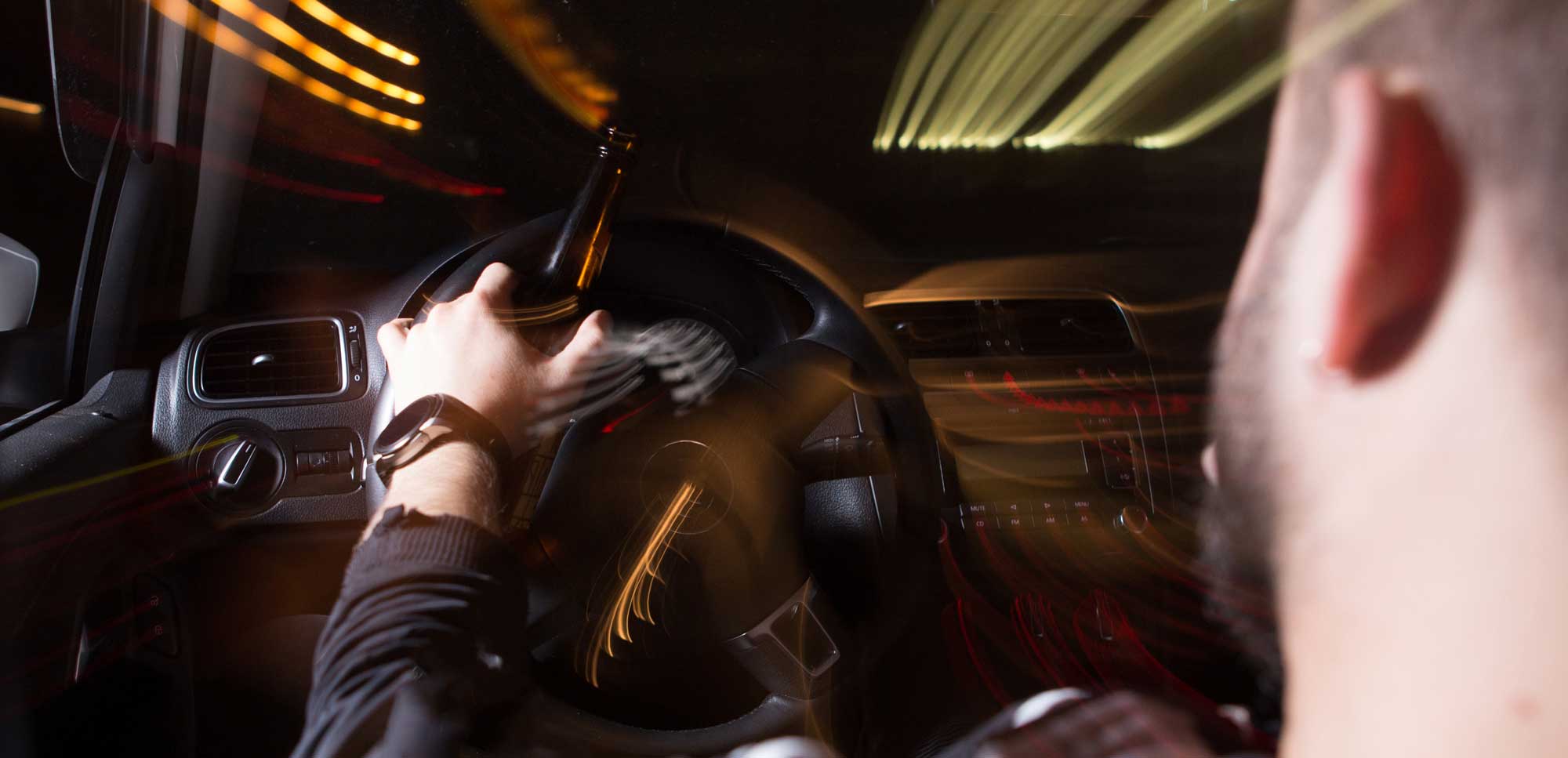 Man driving at night with a beer bottle in his hand not seeing clearly