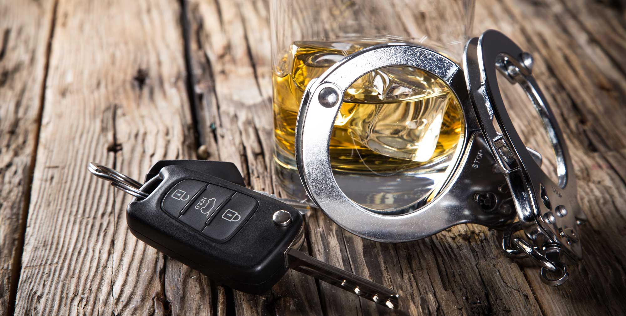 Glass of whiskey, car keys, and handcuffs on a wooden table