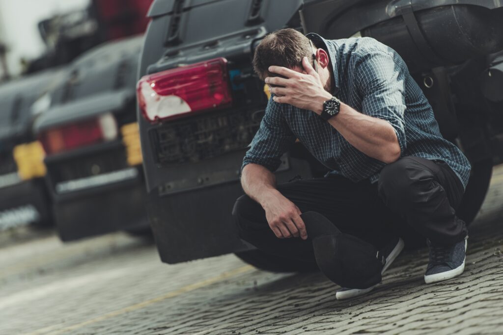 Man crouched down in front of a car with head in hands. man arrested for OVI charge, drunk driving, drinking and driving