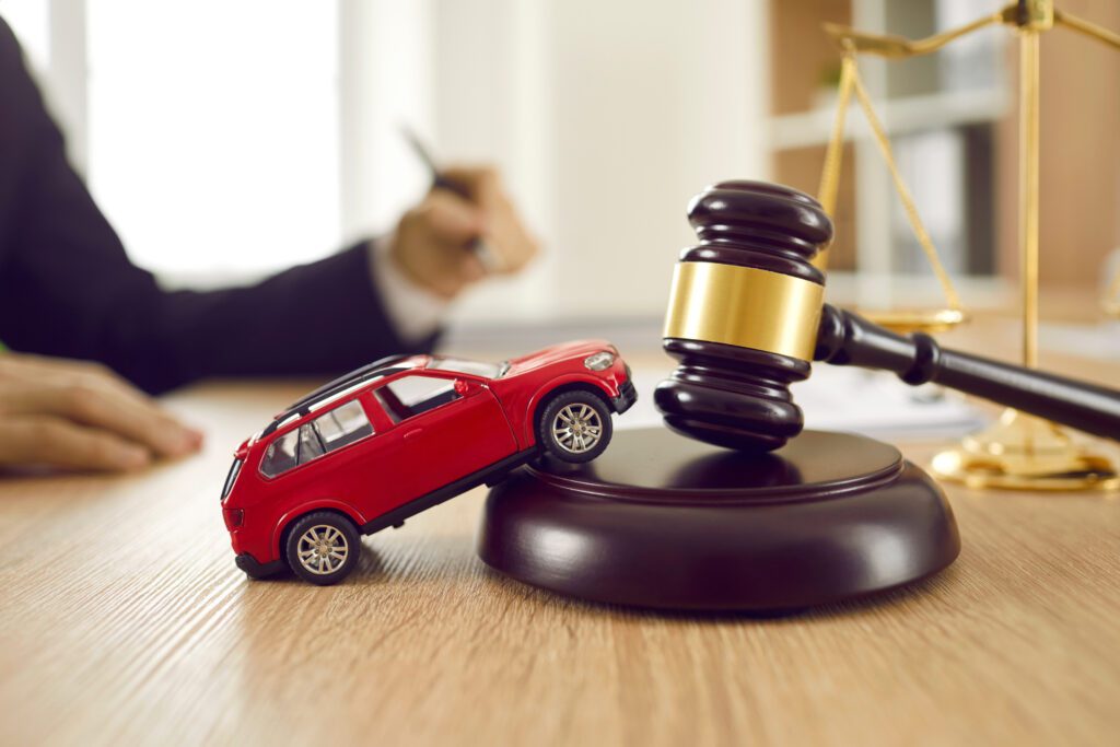 Little red toy automobile on table with sound block and gavel. Small car model on wooden desk with judge's hammer.