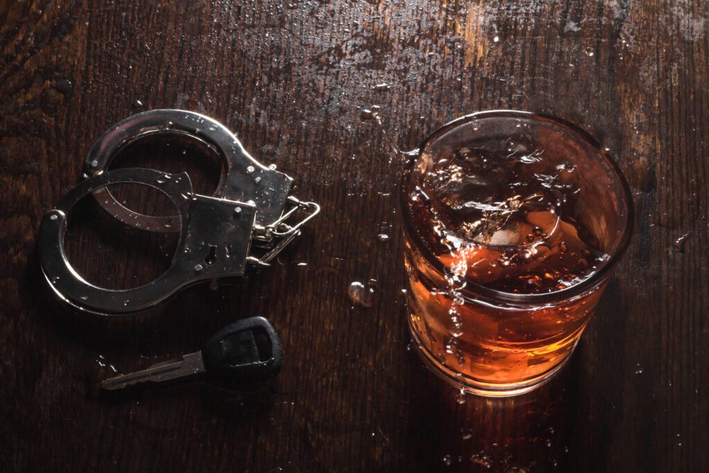 Rocks glass of whisky with handcuffs and keys symbolizing drunk driving arrest, needing OVI lawyer
